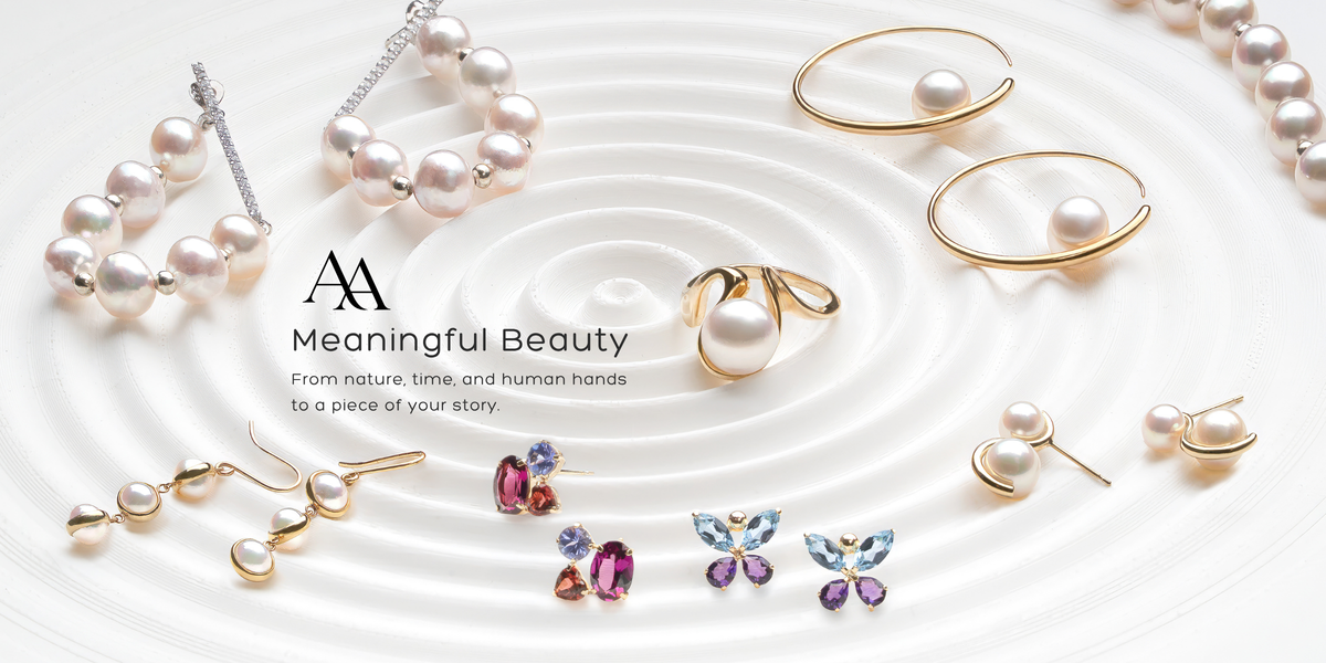 A styled flat-lay of pearl and gold jewelry arranged on a white background with concentric ripple lines. Visible items include pearl strands, pearl drop earrings, a pearl ring, gold hoop earrings with pearls, butterfly stud earrings with pink and blue stones, and a small cluster of pearl and gold pieces.